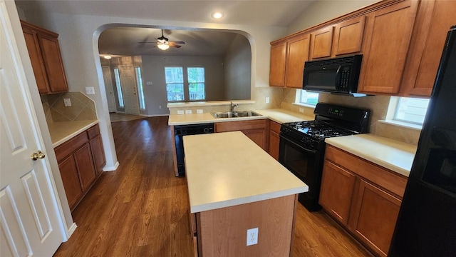 kitchen featuring black appliances, wood finished floors, arched walkways, and a sink