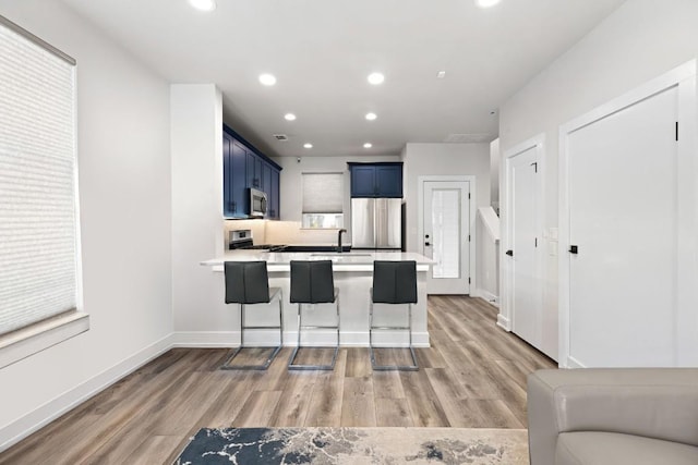 kitchen featuring a peninsula, stainless steel appliances, a sink, light wood finished floors, and blue cabinetry