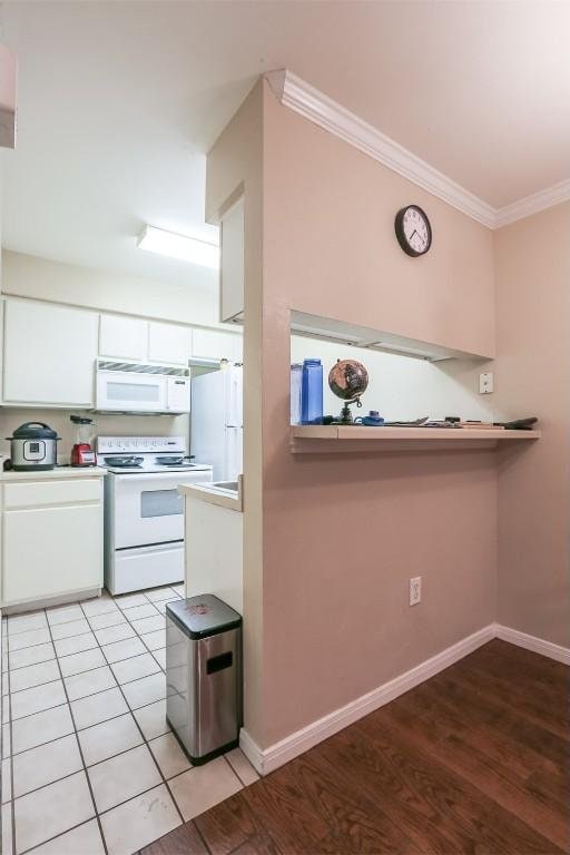 kitchen featuring crown molding, baseboards, white cabinets, and white appliances