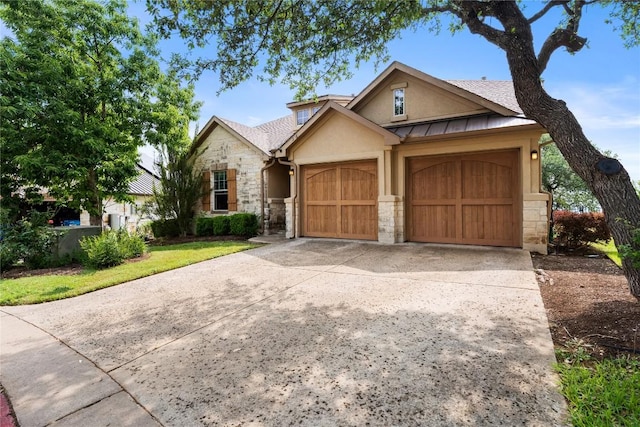 ranch-style house featuring a standing seam roof, a garage, driveway, stone siding, and stucco siding