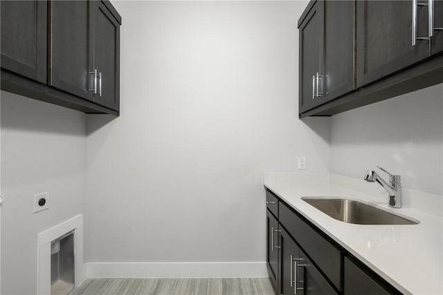 laundry room with electric dryer hookup, light wood-style floors, baseboards, and a sink
