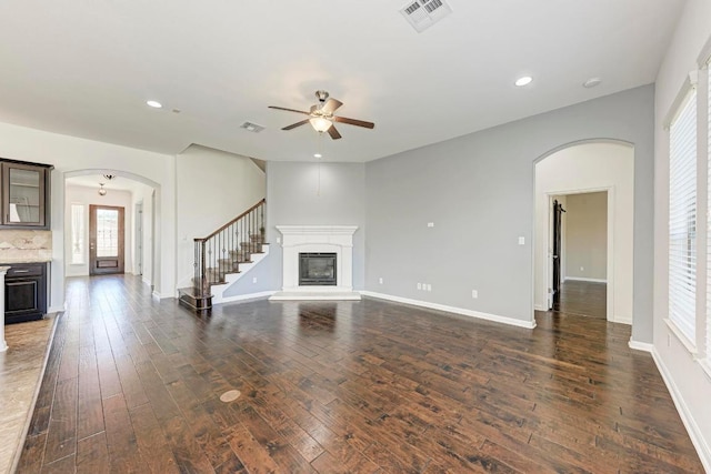 3909 Vinalopo Dr, Austin, TX 78738 - unfurnished living room featuring a glass covered fireplace, arched walkways, a ceiling fan, dark wood-style flooring, and recessed lighting