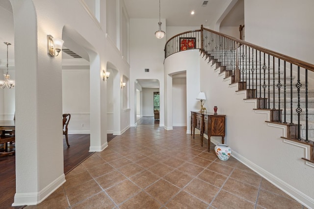 foyer entrance featuring arched walkways, tile patterned floors, a towering ceiling, a notable chandelier, and stairs