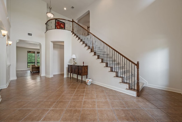 staircase featuring a towering ceiling, visible vents, tile patterned flooring, and arched walkways