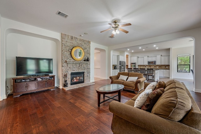 living area with dark wood-style floors, a ceiling fan, visible vents, baseboards, and arched walkways