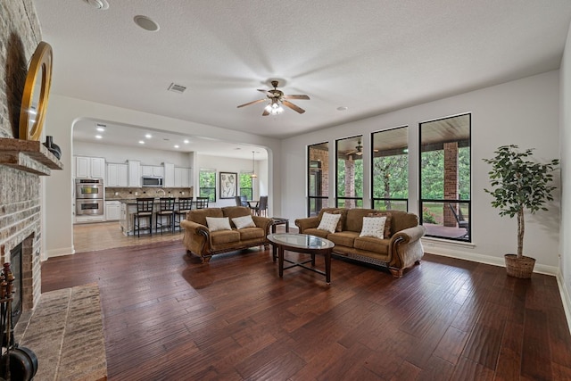 living room featuring dark wood finished floors, arched walkways, ceiling fan, a brick fireplace, and visible vents