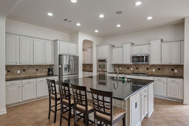 kitchen with a sink, visible vents, stainless steel appliances, arched walkways, and backsplash
