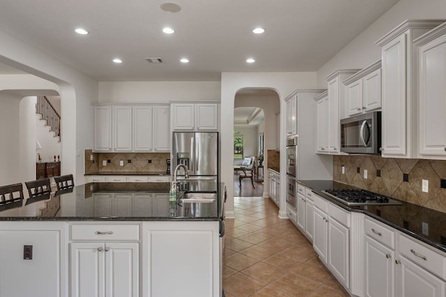 kitchen with recessed lighting, a sink, stainless steel appliances, arched walkways, and an island with sink