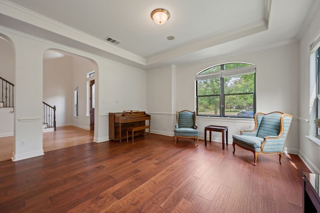 living area featuring stairway, visible vents, a raised ceiling, arched walkways, and wood finished floors