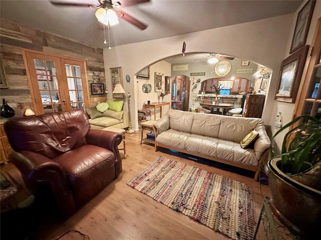 living room with arched walkways, ceiling fan, french doors, and light wood finished floors