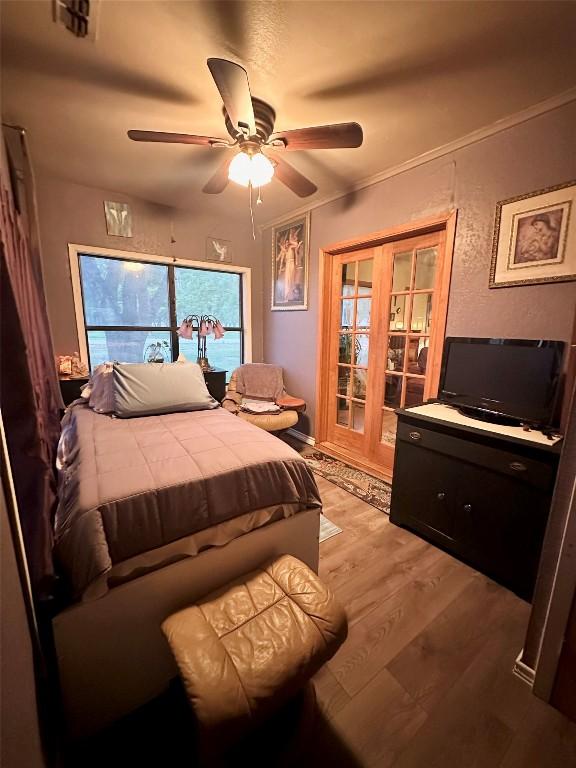 bedroom with light wood finished floors, crown molding, access to exterior, a ceiling fan, and french doors