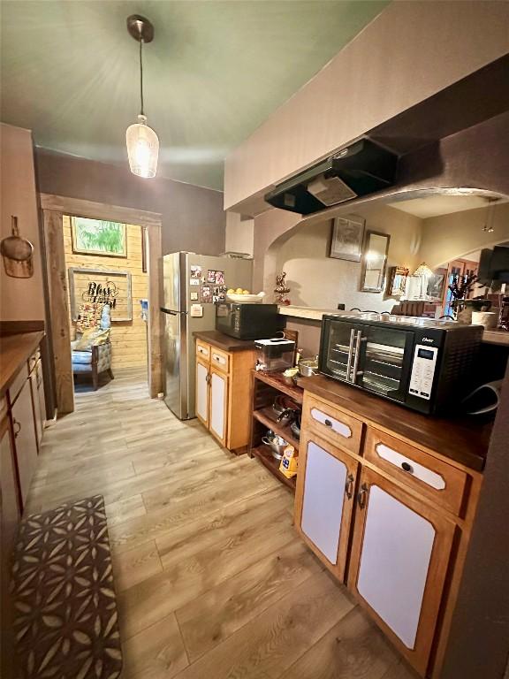 kitchen featuring black microwave, light wood-style floors, dark countertops, and freestanding refrigerator