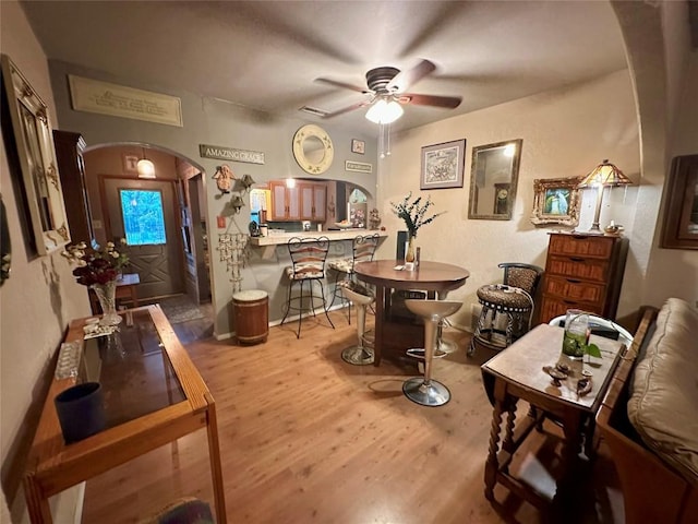 dining area with arched walkways, a ceiling fan, and wood finished floors