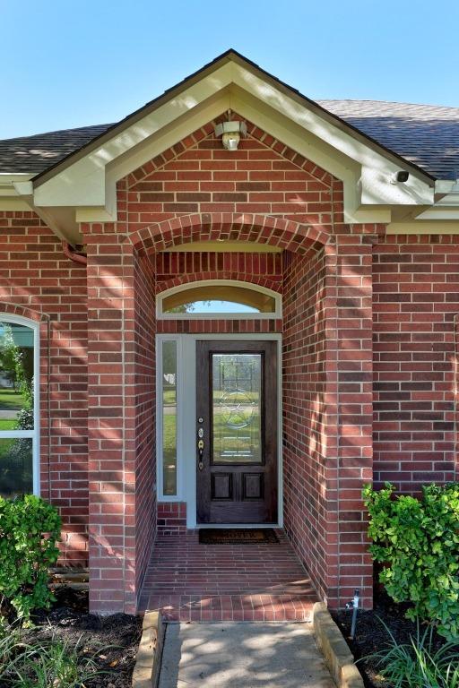 entrance to property featuring a shingled roof and brick siding