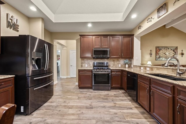 kitchen featuring light stone countertops, decorative backsplash, light wood-style floors, appliances with stainless steel finishes, and a sink