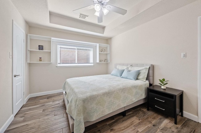bedroom with baseboards, visible vents, wood finished floors, and a tray ceiling