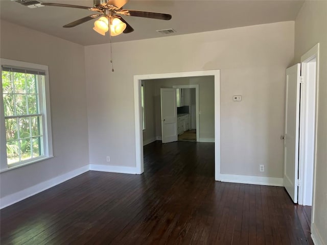spare room featuring dark wood-type flooring, visible vents, a ceiling fan, and baseboards