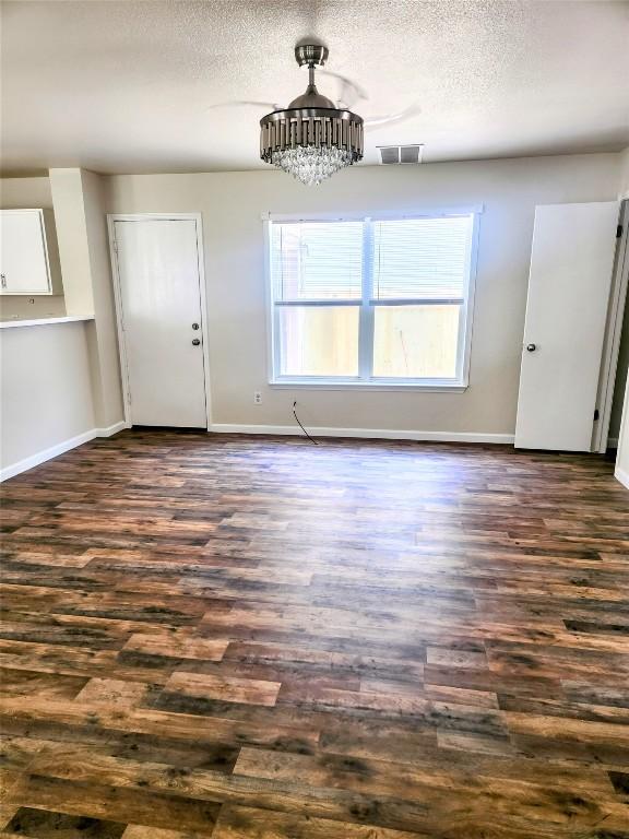 unfurnished dining area with a textured ceiling, dark wood-style flooring, and baseboards