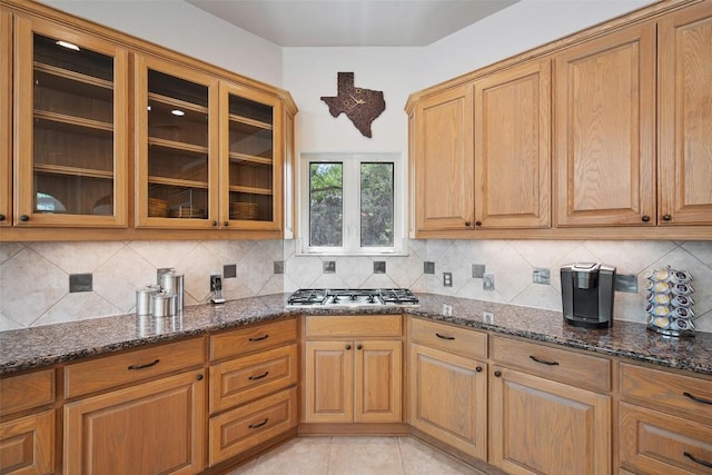 7800 Aspen Highlands Dr, Austin, TX 78746 - kitchen with stainless steel gas stovetop, dark stone counters, tasteful backsplash, glass insert cabinets, and brown cabinetry