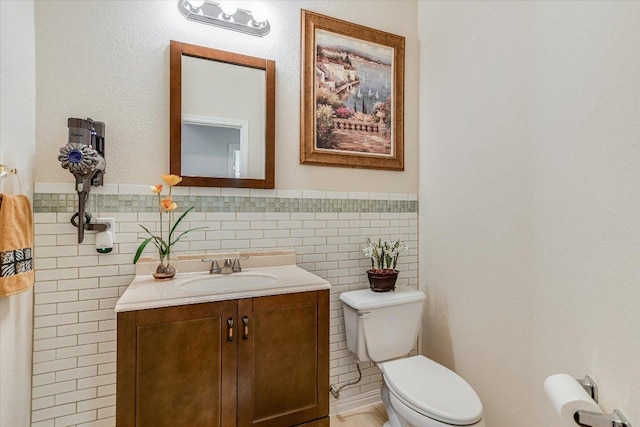 bathroom featuring tile walls, wainscoting, toilet, and vanity