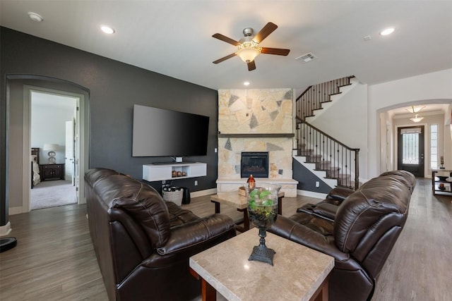1728 Siena Sunset Rd, Leander, TX 78641 - living room featuring arched walkways, stairway, a stone fireplace, a ceiling fan, and wood finished floors