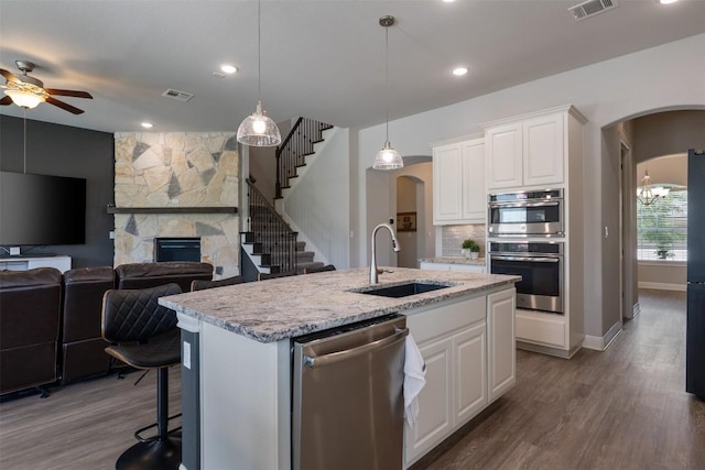 1728 Siena Sunset Rd, Leander, TX 78641 - kitchen featuring appliances with stainless steel finishes, arched walkways, ceiling fan, a stone fireplace, and dark wood-style flooring