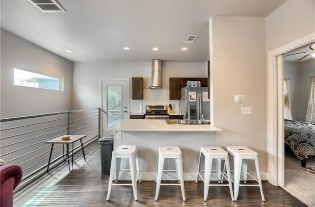 kitchen with wall chimney range hood, a breakfast bar area, backsplash, and appliances with stainless steel finishes