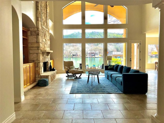 living area featuring a towering ceiling, a ceiling fan, baseboards, and a fireplace