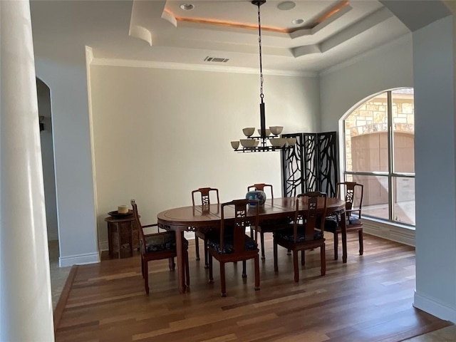 dining space with a notable chandelier, arched walkways, wood finished floors, a tray ceiling, and visible vents