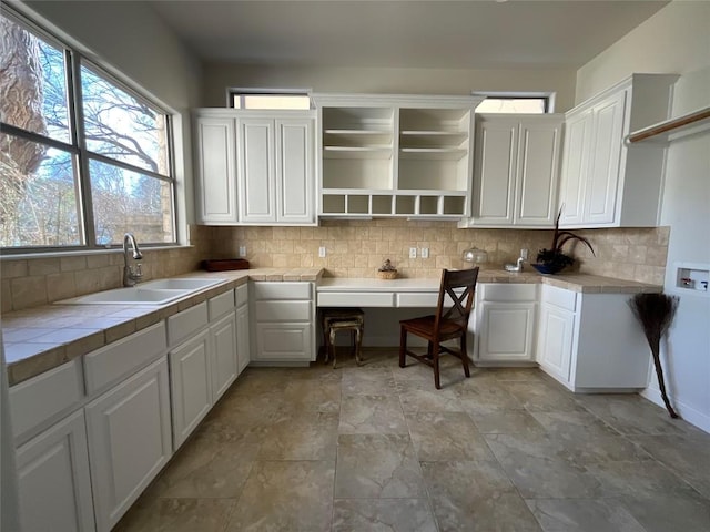 kitchen with tile countertops, open shelves, a sink, and tasteful backsplash