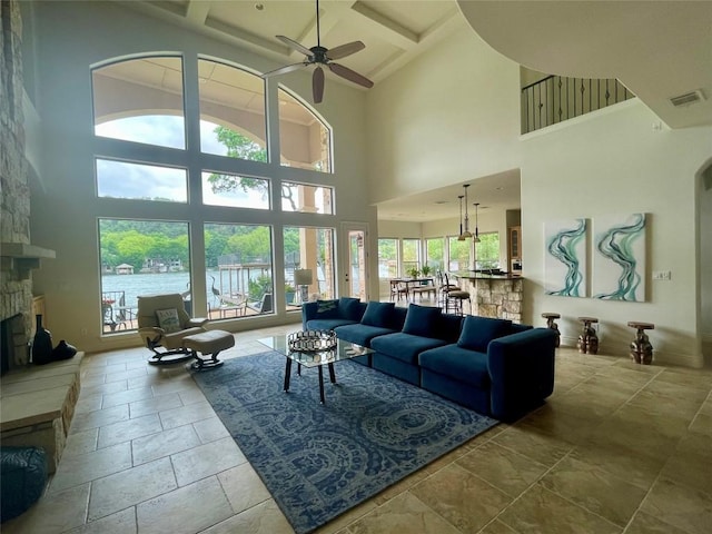 living room featuring a high ceiling, a stone fireplace, and ceiling fan