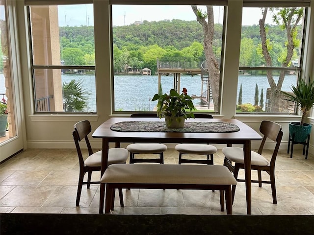 dining area featuring a water view, baseboards, a forest view, and stone tile flooring