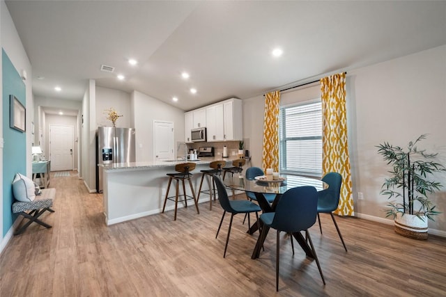 dining space featuring recessed lighting, light wood-style floors, vaulted ceiling, baseboards, and visible vents