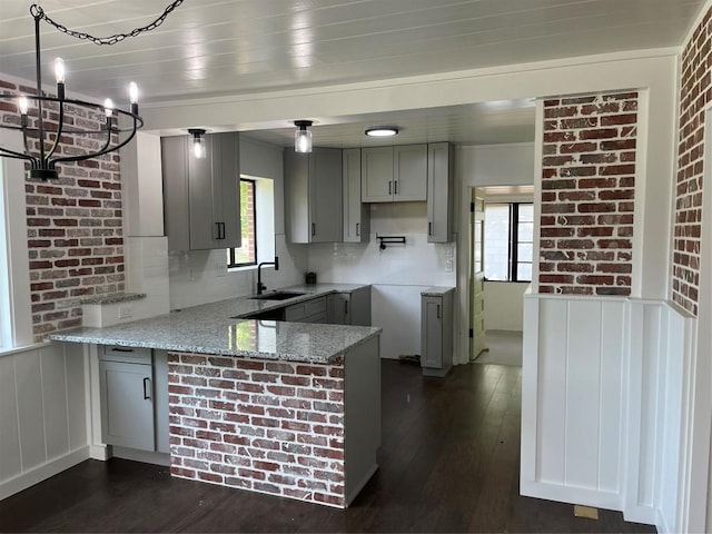 5611 Joe Sayers Ave, Austin, TX 78756 - kitchen featuring a peninsula, gray cabinetry, light stone countertops, dark wood finished floors, and tasteful backsplash