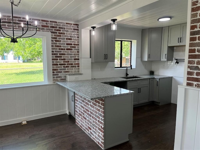 5611 Joe Sayers Ave, Austin, TX 78756 - kitchen with a sink, a peninsula, light stone countertops, dark wood-style flooring, and brick wall