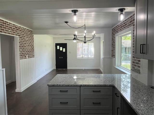 5611 Joe Sayers Ave, Austin, TX 78756 - kitchen featuring a peninsula, light stone countertops, brick wall, dark wood-style flooring, and gray cabinets