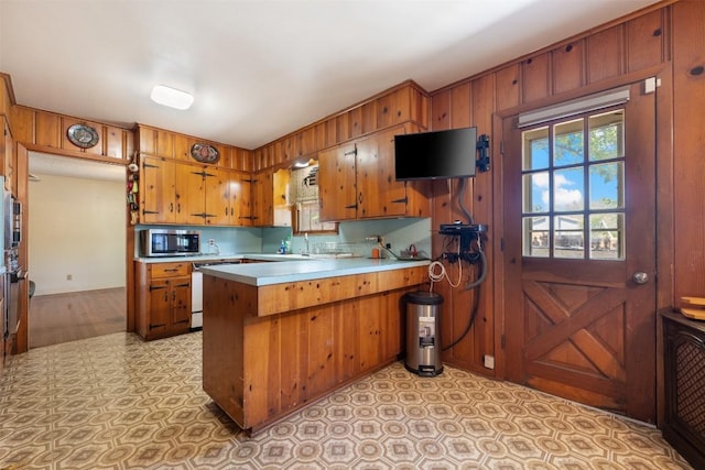 kitchen with stainless steel microwave, brown cabinetry, light countertops, a peninsula, and dishwashing machine