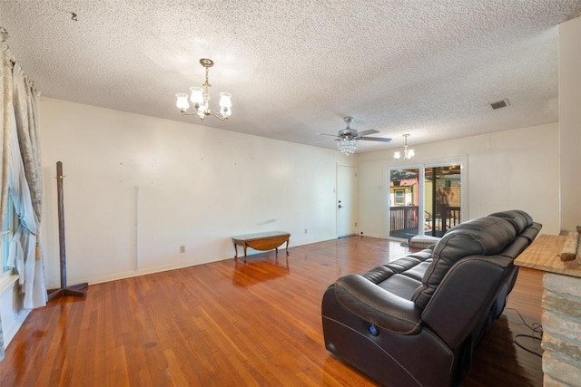 living area with visible vents, wood finished floors, ceiling fan with notable chandelier, and a textured ceiling