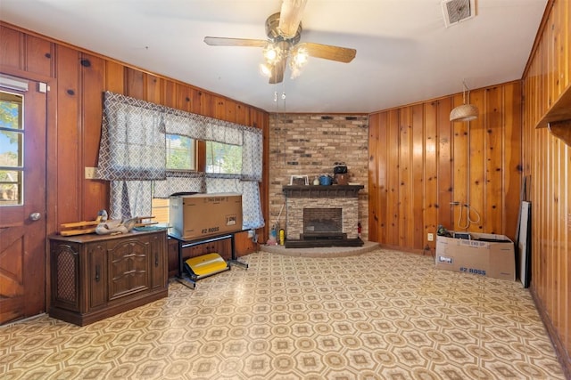 living room featuring visible vents, ceiling fan, wood walls, and a fireplace