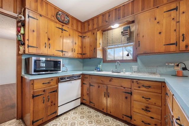 kitchen with stainless steel microwave, brown cabinetry, light countertops, dishwasher, and a sink