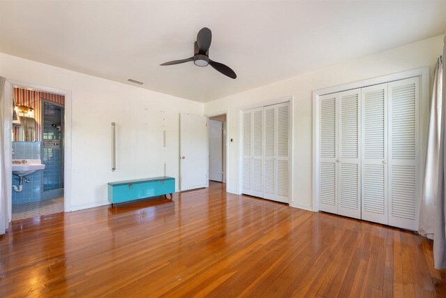 unfurnished bedroom featuring two closets, visible vents, baseboards, wood finished floors, and a ceiling fan