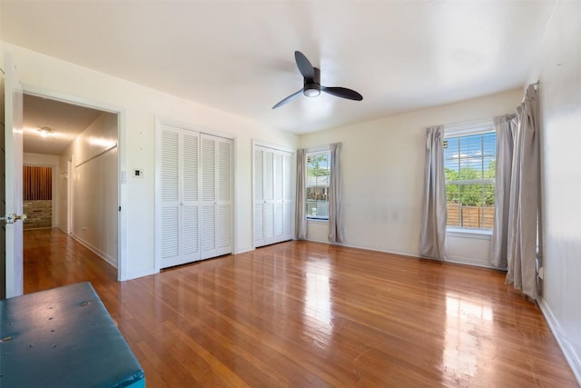 unfurnished bedroom with multiple windows, multiple closets, wood finished floors, and baseboards