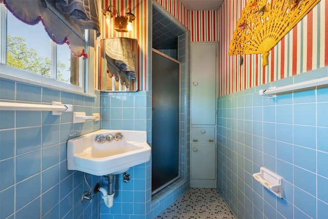 full bathroom featuring a sink, a wainscoted wall, a stall shower, wallpapered walls, and tile walls