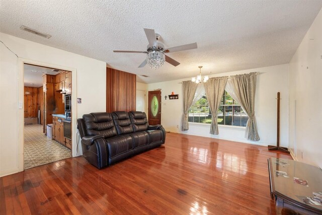 living area featuring visible vents, hardwood / wood-style flooring, ceiling fan with notable chandelier, and a textured ceiling