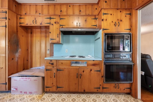 kitchen featuring brown cabinetry, black appliances, under cabinet range hood, and light countertops