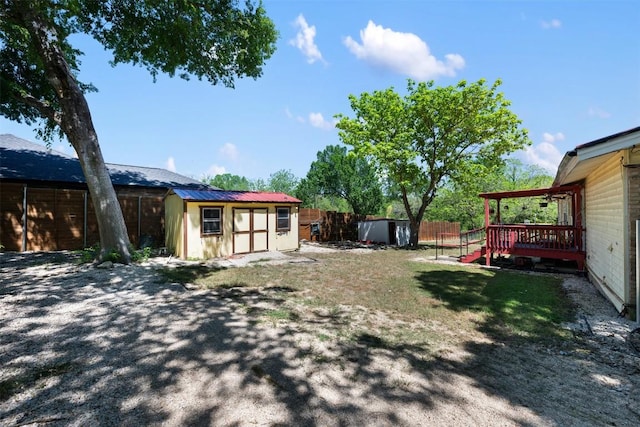 view of yard featuring an outdoor structure, a wooden deck, a storage unit, and a fenced backyard