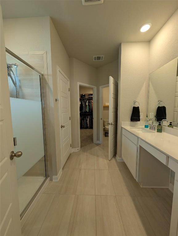 full bath featuring a walk in closet, visible vents, a shower stall, and vanity