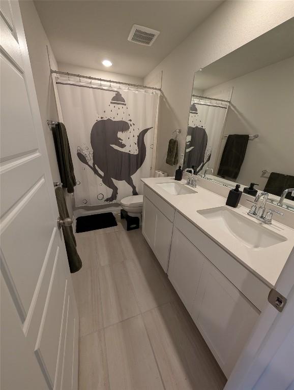 bathroom with a sink, toilet, visible vents, and double vanity