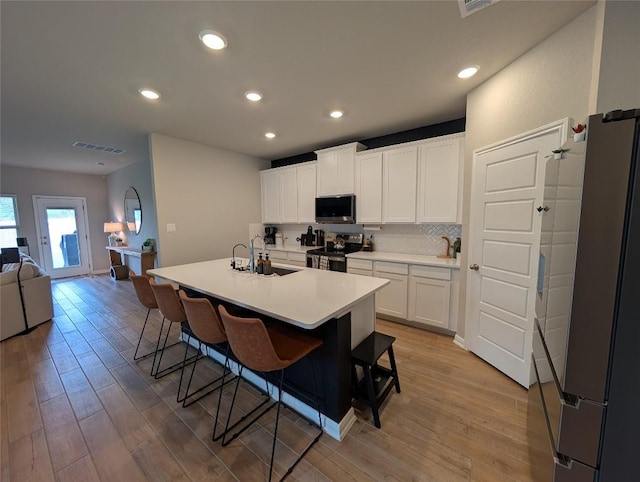 kitchen featuring a breakfast bar area, a sink, appliances with stainless steel finishes, visible vents, and open floor plan
