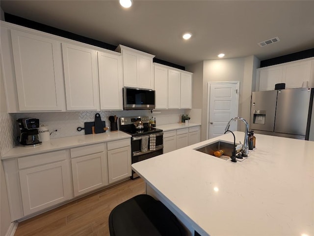kitchen with light wood-style flooring, stainless steel appliances, a sink, white cabinetry, and visible vents